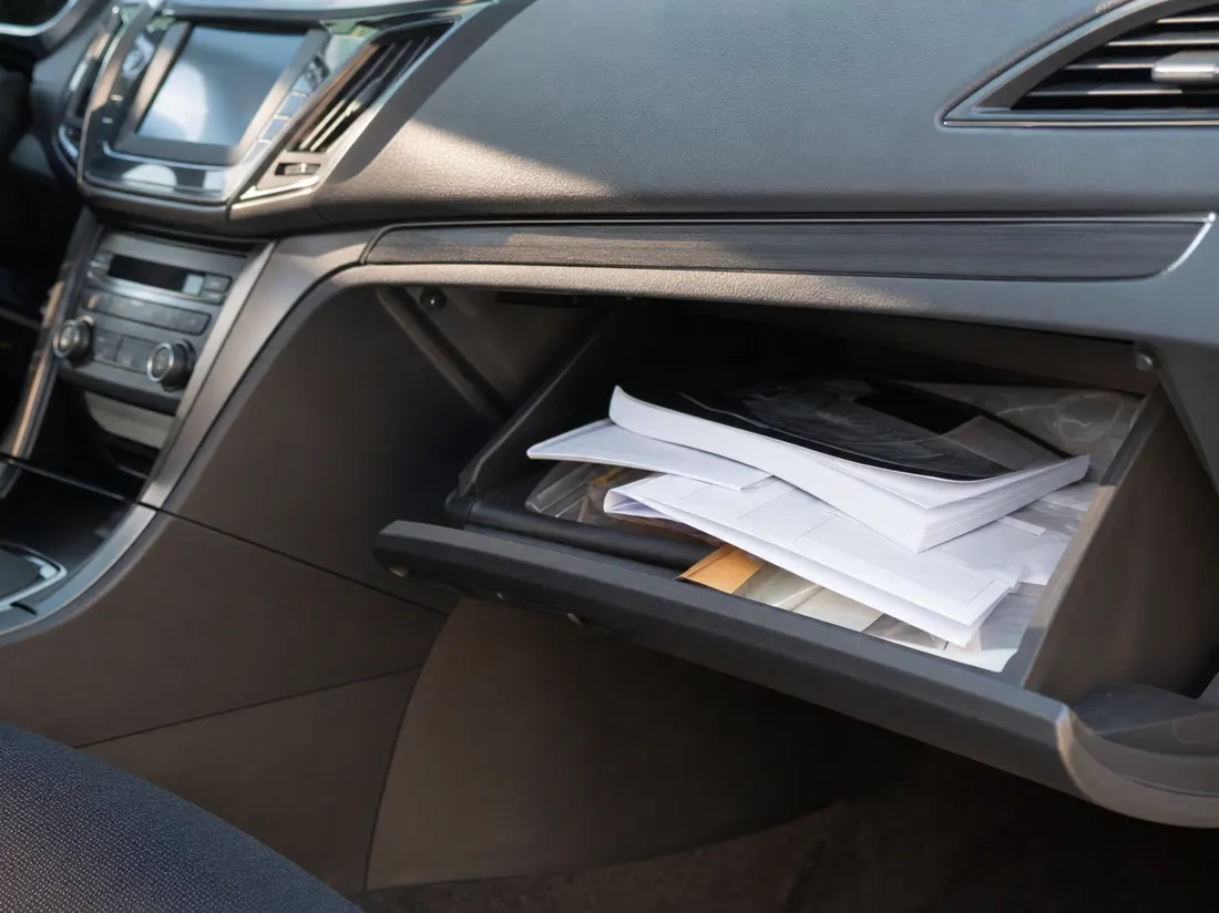 An open glovebox with a folded manual and loose papers - selling a car without the title