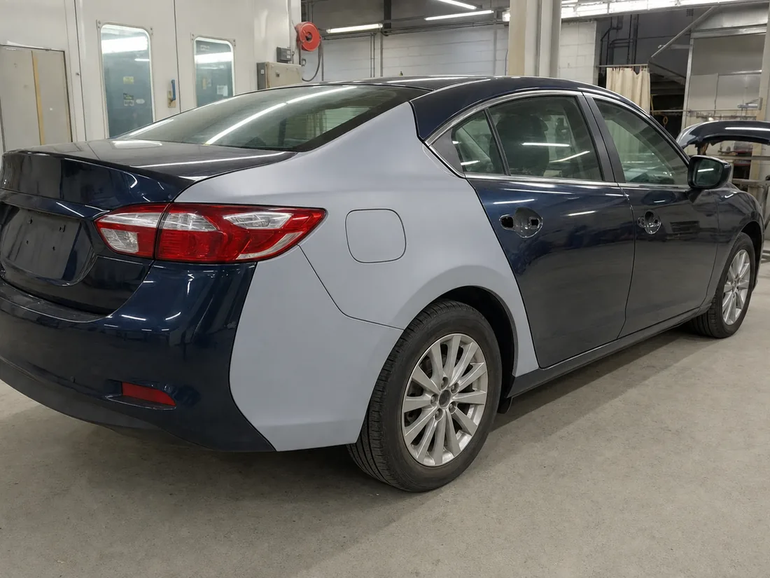 A sedan part-way through body repair in a workshop, one quarter panel in fresh grey primer and the rest in finished paint