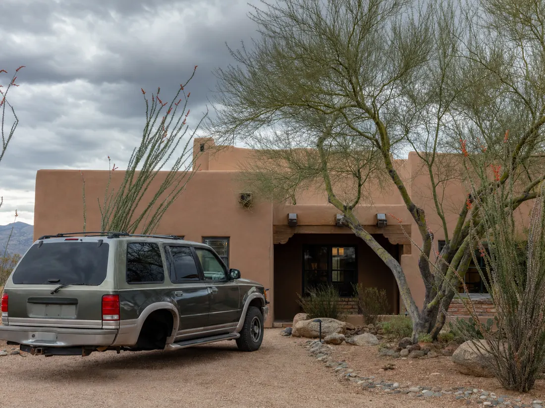 Older SUV at a Tucson adobe-style home with ocotillo and palo verde trees, monsoon clouds building - selling a car in Tucson