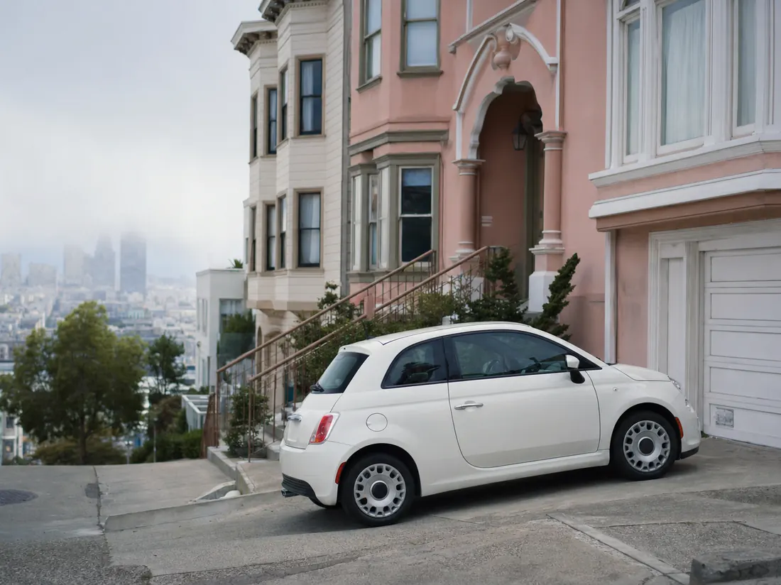 Compact car parked on a steep San Francisco street beside pastel Victorian homes, fog burning off - selling a car in San Francisco