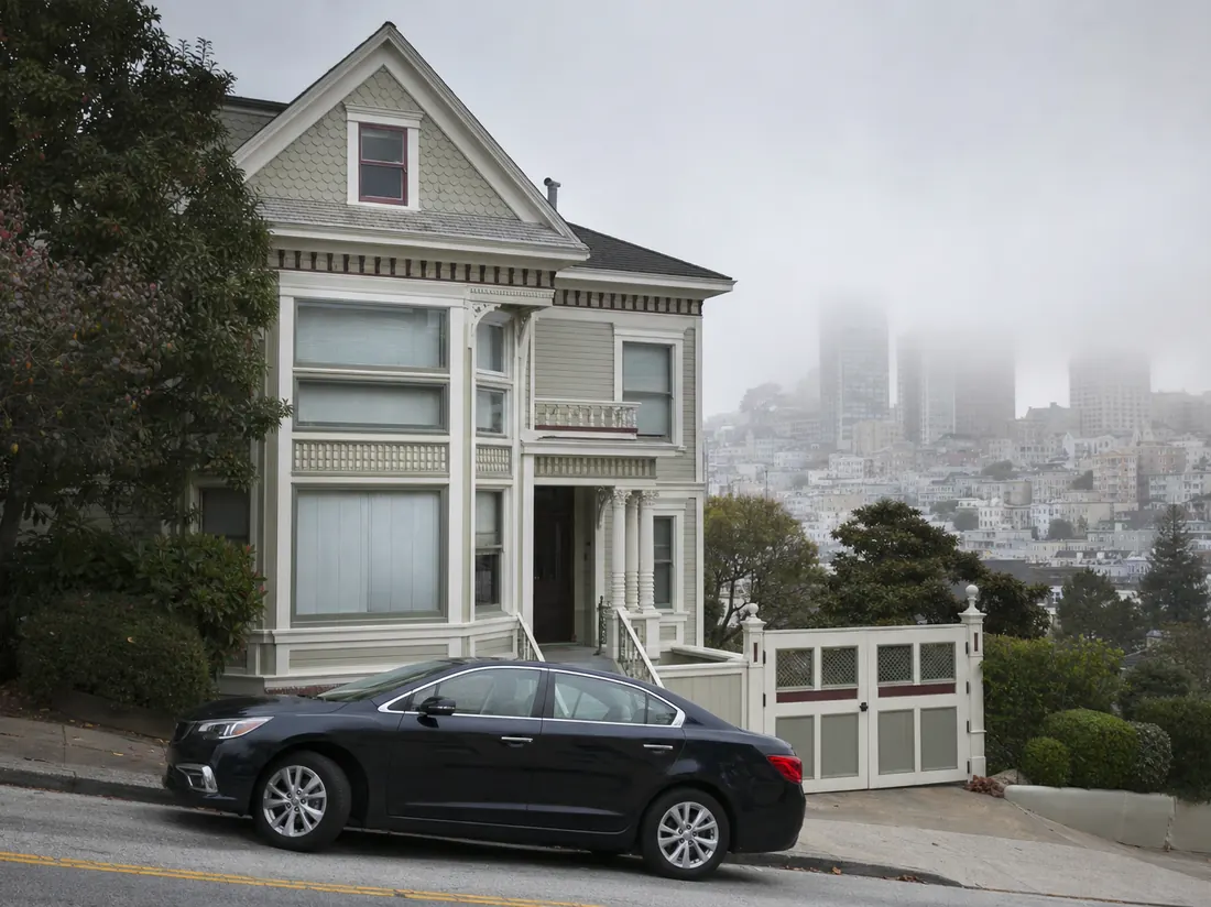 Sedan parked in front of a Victorian-style Northern California home with a steep street and bay fog rolling in - selling a car in California