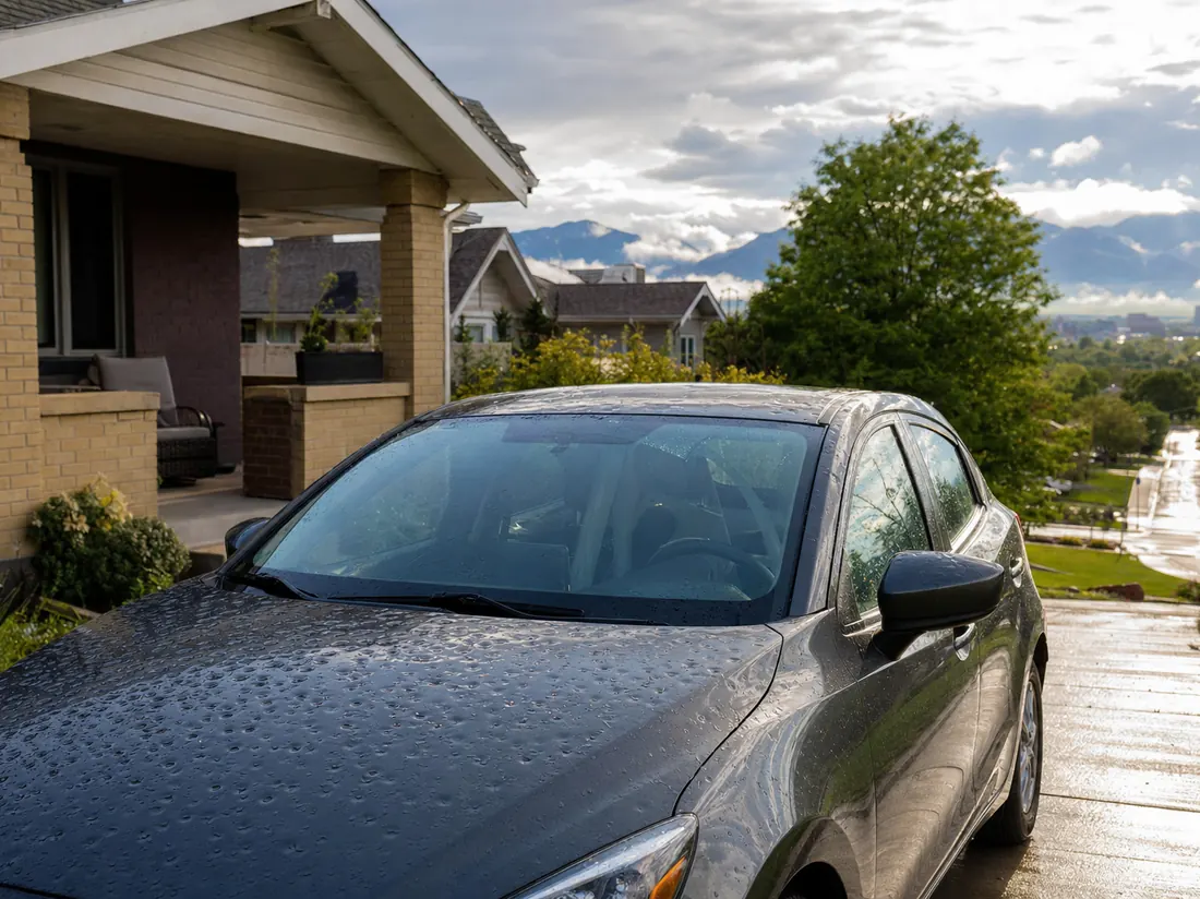 Hatchback with hail dimples on the hood at a Denver bungalow with the front range visible down the street - selling a car in Denver