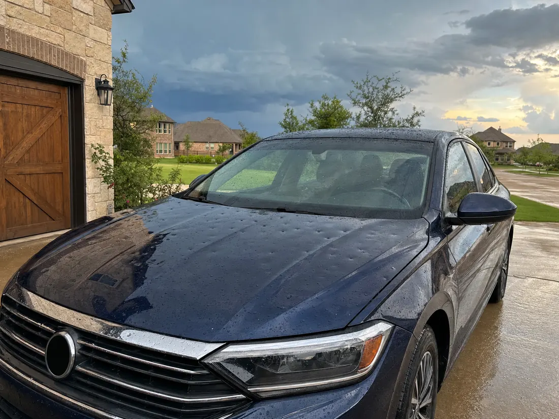 Sedan with hail dents in a North Texas driveway after a storm, ready to sell