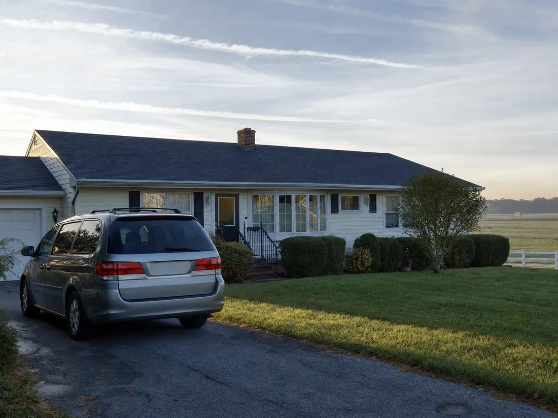 Minivan in the driveway of a one-story ranch home near Dover Delaware with flat farm fields beyond the backyard - selling a car in Dover