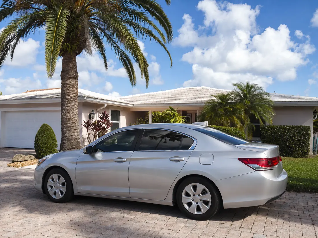 Sedan in the driveway of a Florida home with palm trees - selling a car in Florida