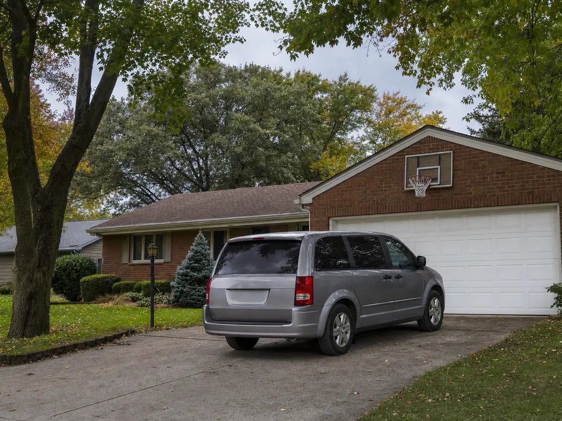 Minivan in the driveway of a brick ranch home in Fort Wayne Indiana with a basketball hoop over the garage and mature maples - selling a car in Fort Wayne
