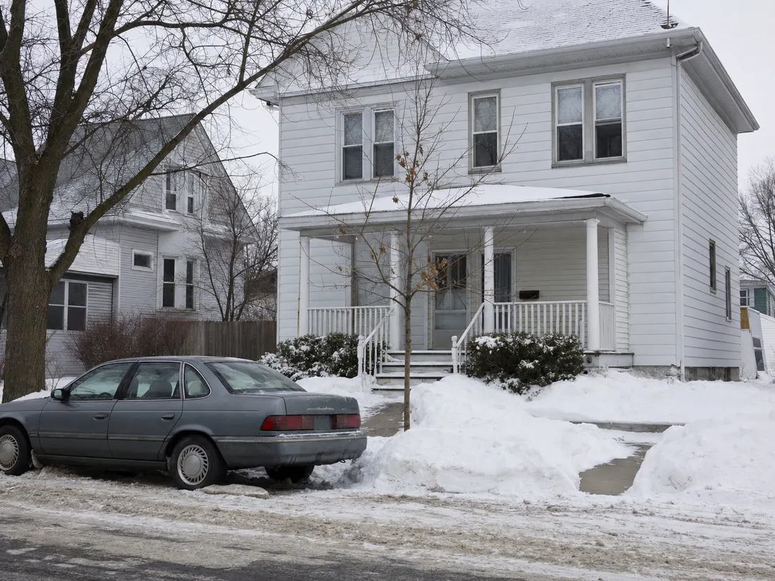 Older sedan beside a two-story frame house in South Bend Indiana with snow shoveled into hard banks along the walk - selling a car in South Bend