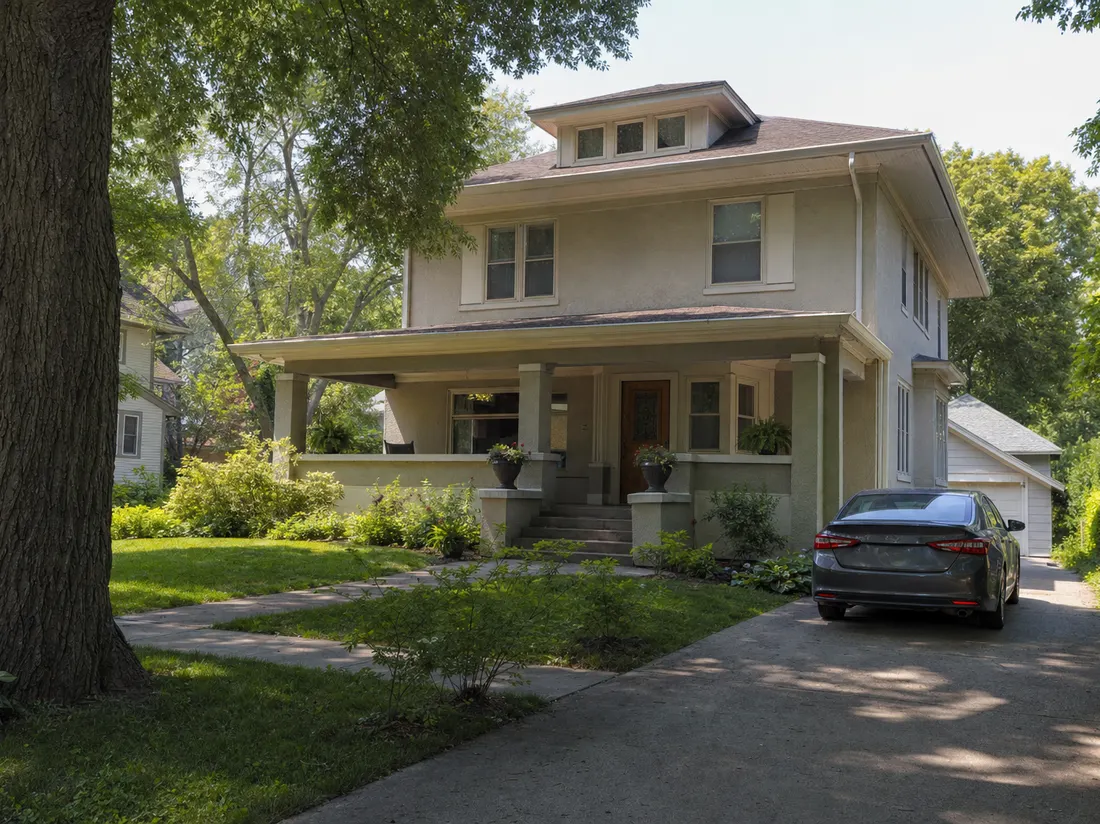 Sedan in the driveway of an American foursquare home in Des Moines Iowa with a wide porch and mature elm - selling a car in Des Moines