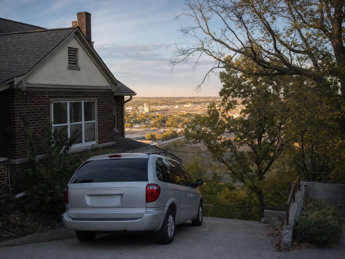 Minivan in the sloped driveway of an older hillside home in Sioux City Iowa with bur oaks and a big prairie sky - selling a car in Sioux City