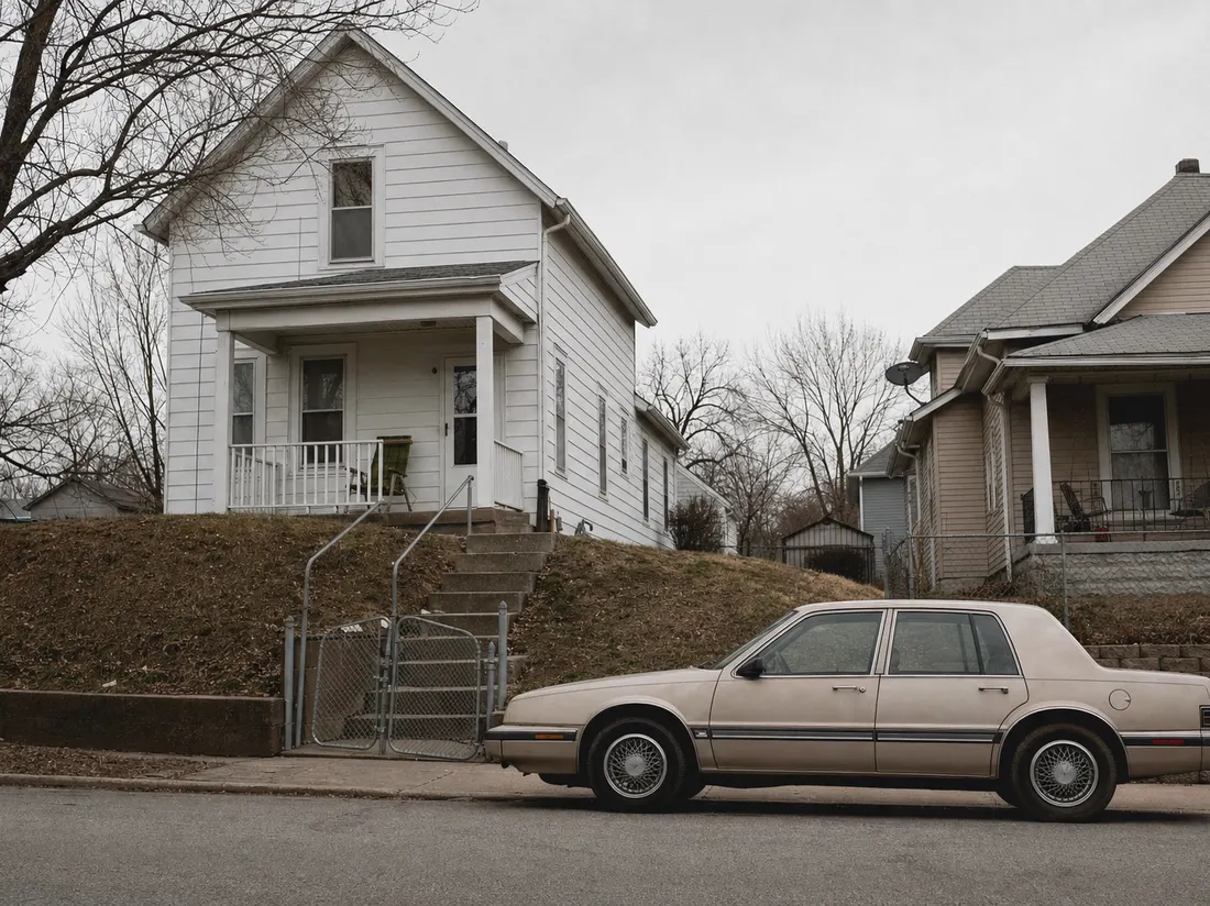 Older sedan beside a frame shirtwaist house in Kansas City Kansas with a steep front lawn and chain-link gate - selling a car in Kansas City