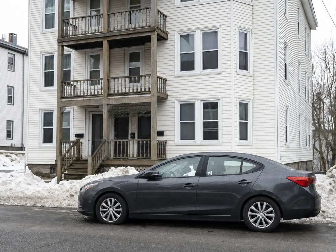 Sedan parked on the street by a mill-town triple-decker in Lewiston Maine with snowbanks along the curb - selling a car in Lewiston