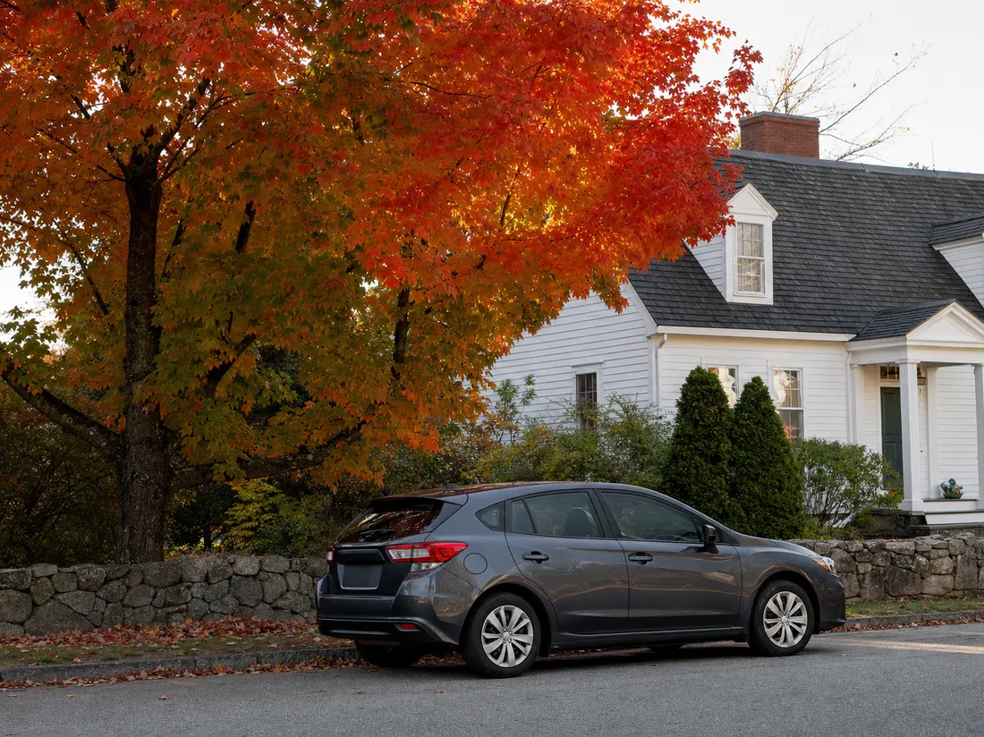 Hatchback beside a white clapboard New England cape in Portland Maine with a stone wall and blazing fall maples - selling a car in Portland