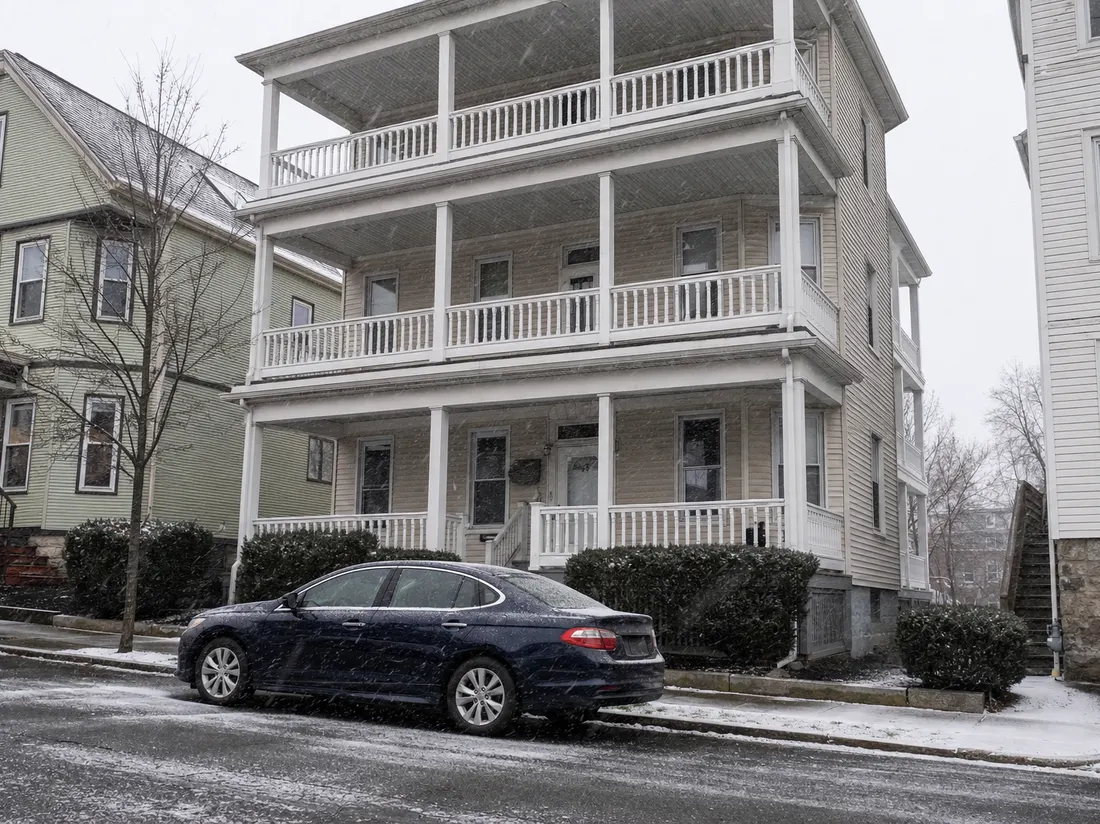 Sedan parked in front of a three-decker home in Worcester Massachusetts with porches stacked three high and snow flurries - selling a car in Worcester