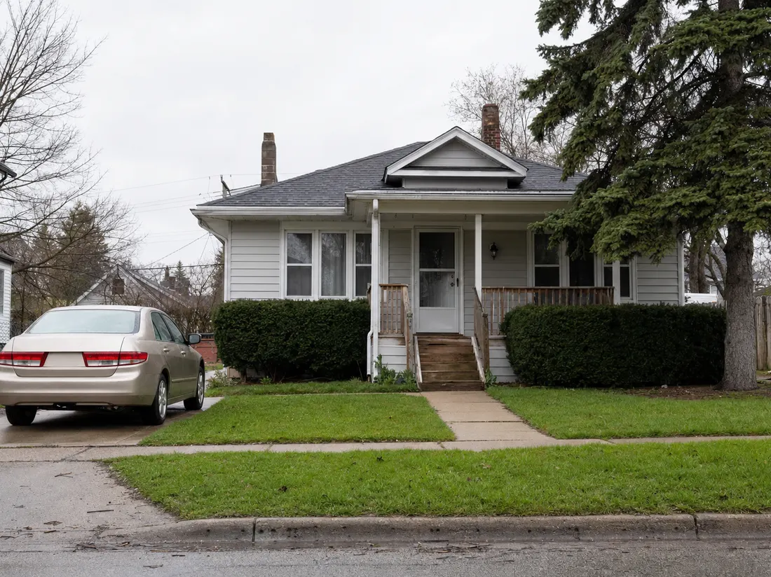 Sedan beside a modest bungalow in Lansing Michigan with a tidy lawn and gray spring thaw sky - selling a car in Lansing