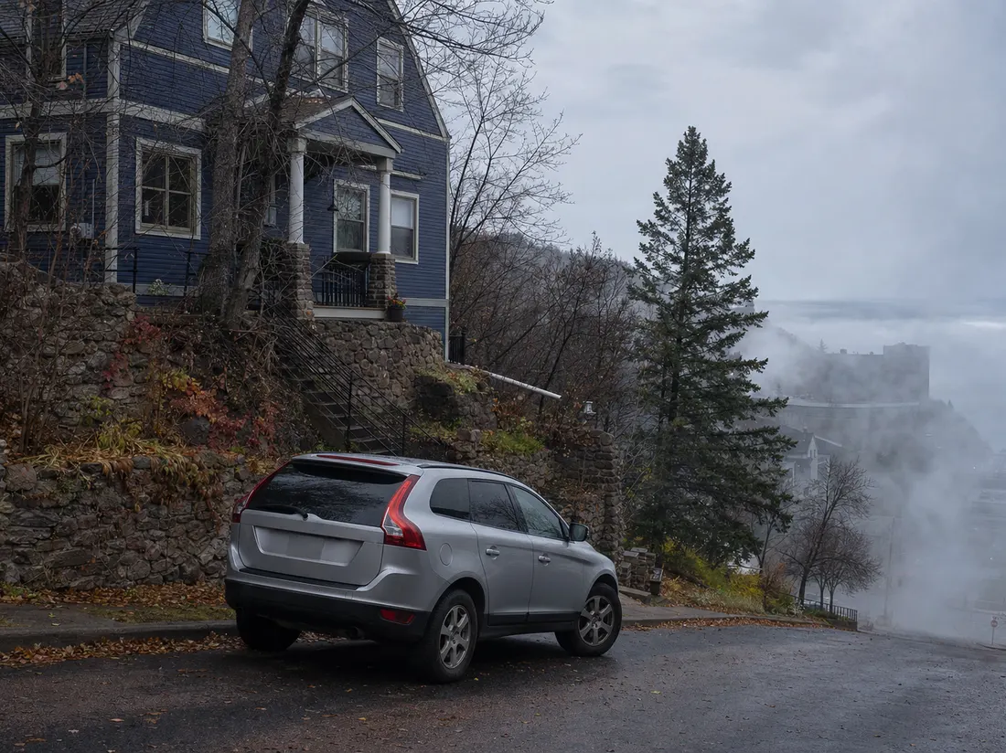 Older crossover on a steep Duluth Minnesota street beside a hillside home with lake fog rolling up the block - selling a car in Duluth