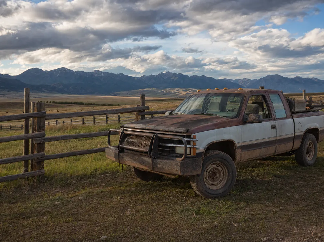 Well-used ranch truck by a fence line in Montana with big sky and distant mountain ranges, dramatic clouds - selling a car in Montana
