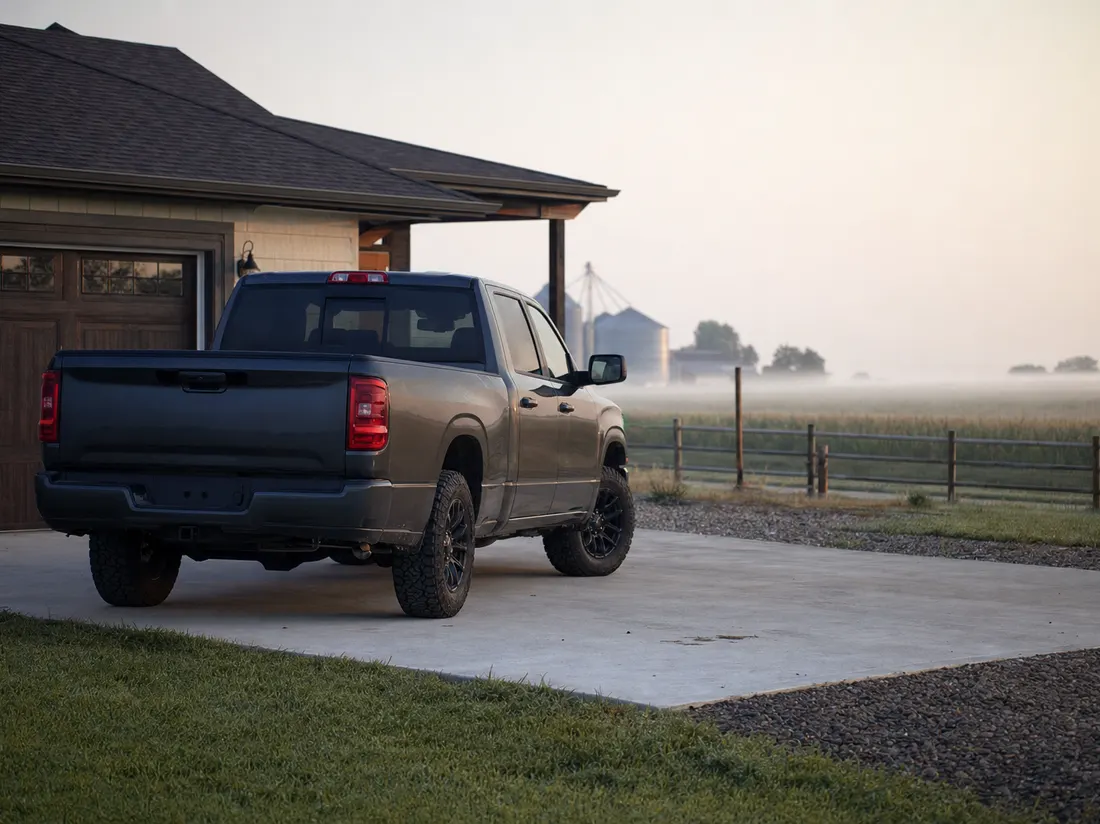 Pickup on the concrete drive of a farm-edge ranch home near Grand Island Nebraska with grain fields past the fence line - selling a car in Grand Island