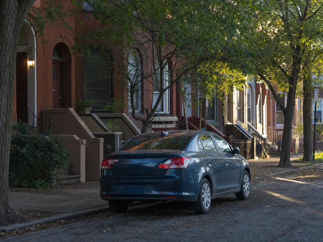 Sedan parked at the curb of a brick rowhouse block in Newark New Jersey with stoops and street trees - selling a car in Newark
