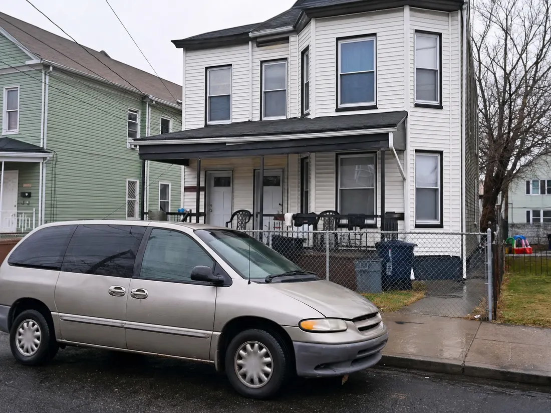 Older minivan outside a two-family frame house in Paterson New Jersey with a small porch and chain-link fence - selling a car in Paterson