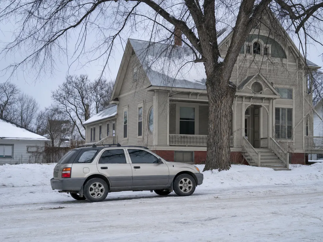 Older crossover by a prairie Victorian home in Grand Forks North Dakota with bare elms and packed snow - selling a car in Grand Forks