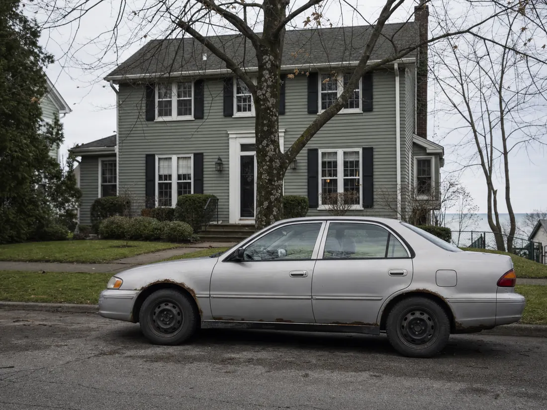 Older sedan with rust at the wheel wells outside a Cleveland colonial under a lake-effect sky - selling a car in Cleveland