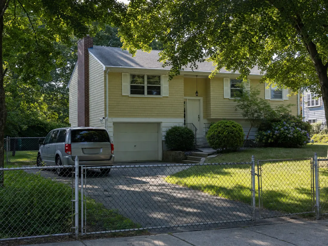 Minivan in the driveway of a 1960s split-level home in Warwick Rhode Island with a chain-link fence and mature maples - selling a car in Warwick