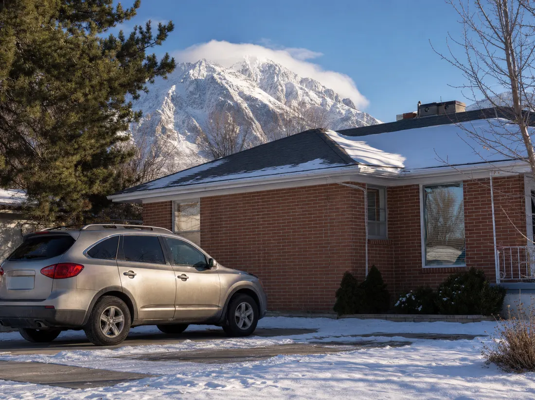 Older crossover beside a brick bungalow in Ogden Utah with Ben Lomond peak snow-covered behind - selling a car in Ogden