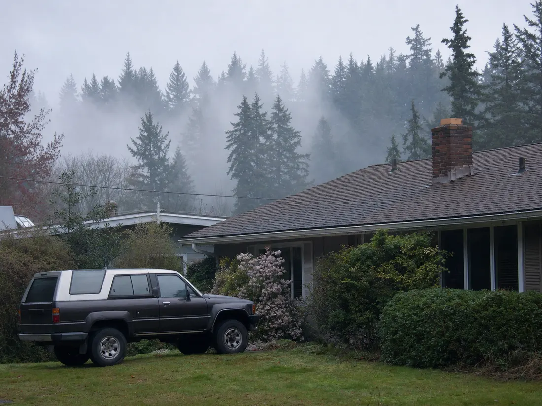 Older SUV beside a rambler home in Everett Washington with Puget Sound mist rolling through the evergreens - selling a car in Everett