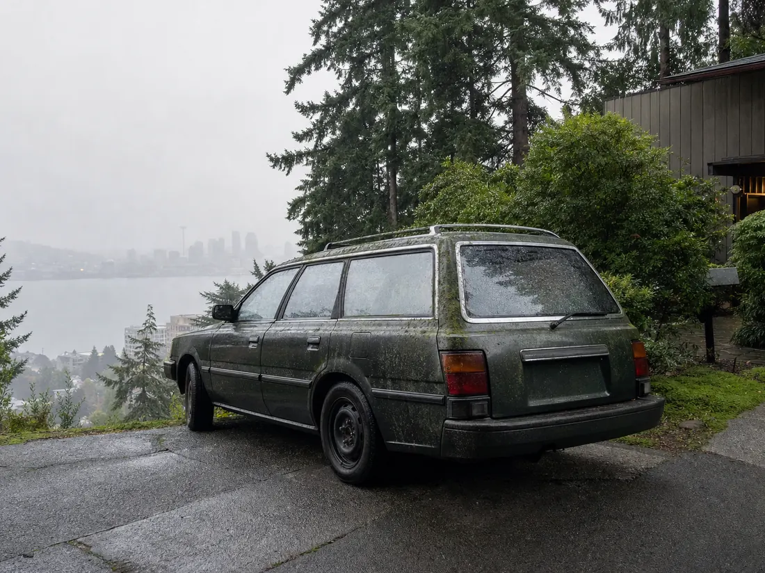 Moss-tinged older wagon on a sloped Seattle driveway with tall firs and drizzle - selling a car in Seattle