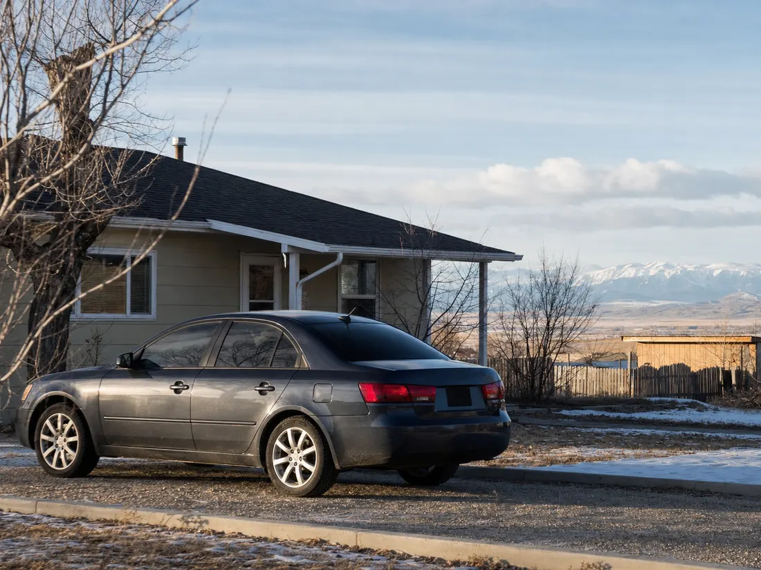 Sedan parked by a bungalow in Laramie Wyoming with bare high-plains light and the Snowy Range faint on the horizon - selling a car in Laramie