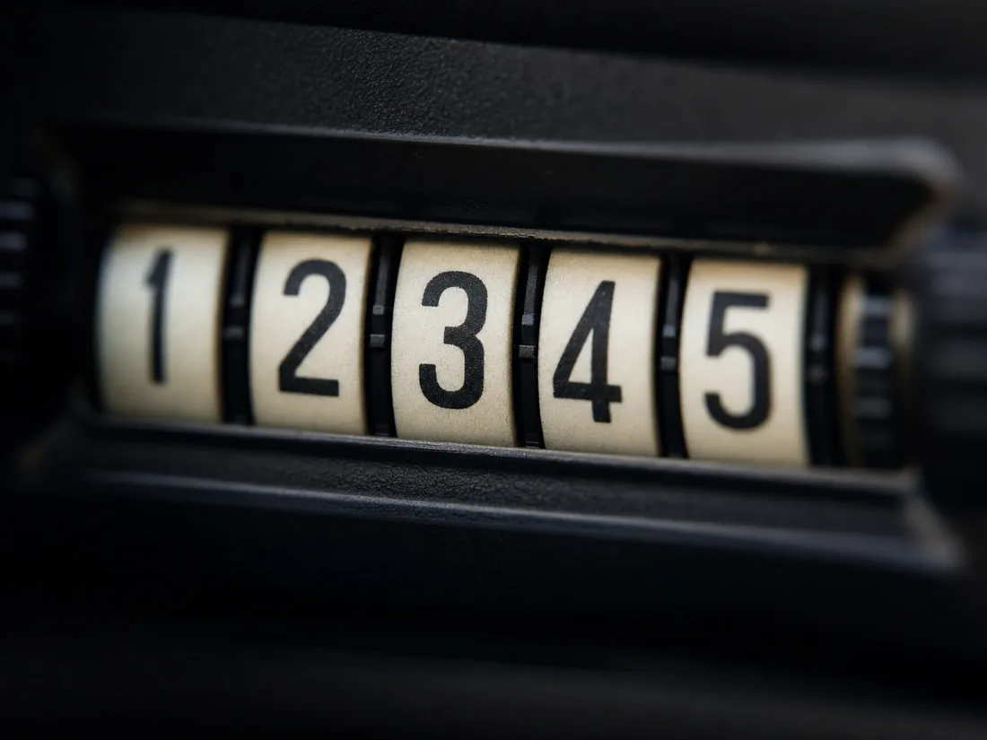 Macro shot of an analog odometer, white number drums sharp against a dark dashboard - the rolling digits the 2002 study tried to count