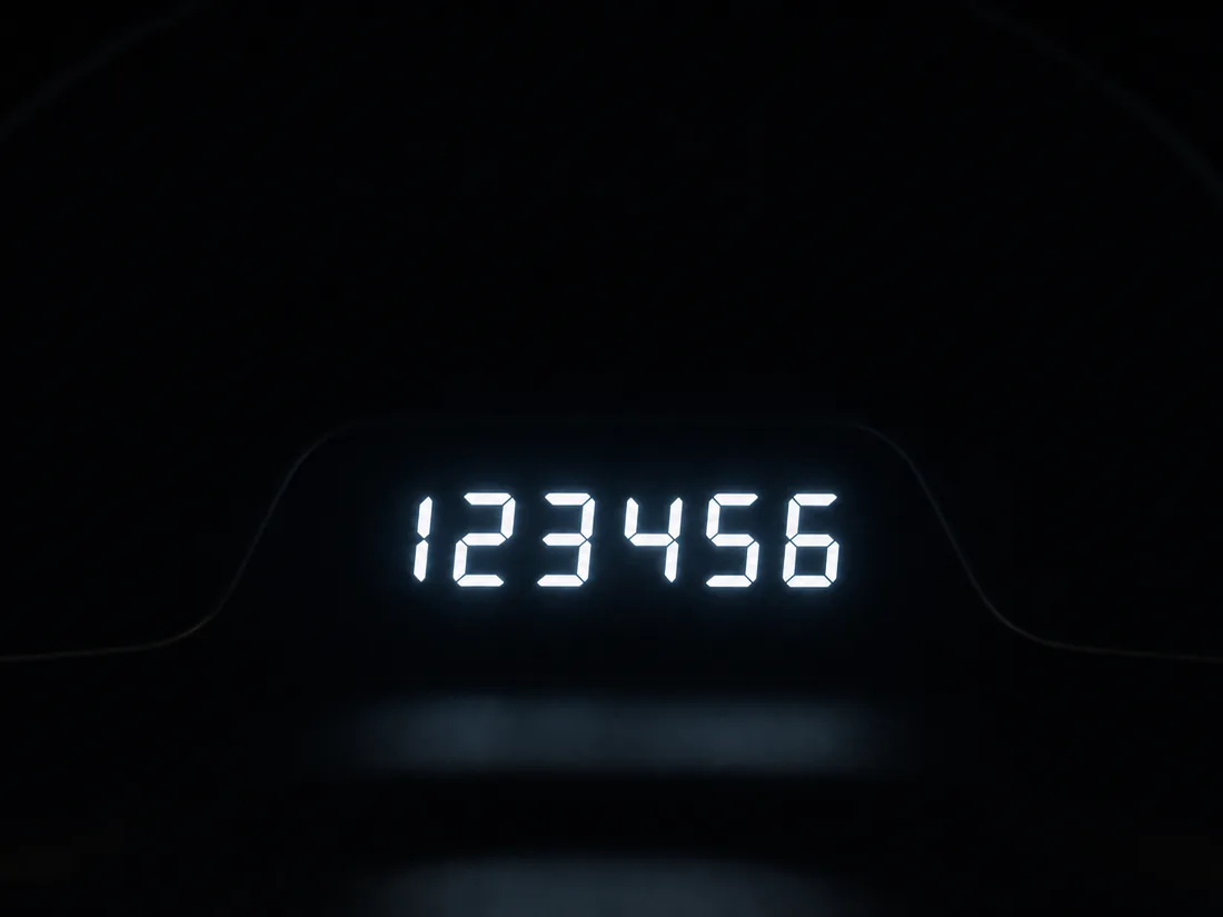 Digital instrument cluster at night showing a six-figure odometer readout - the number federal law says must be disclosed for twenty years